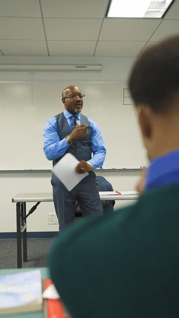A teacher addressing the class from the whiteboard